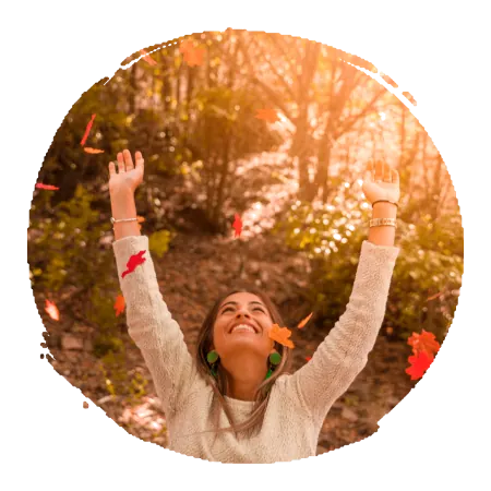 femme brune heureuse et souriante, les bras écartés tendus vers le ciel, dans une forêt en automne, en fin de journée